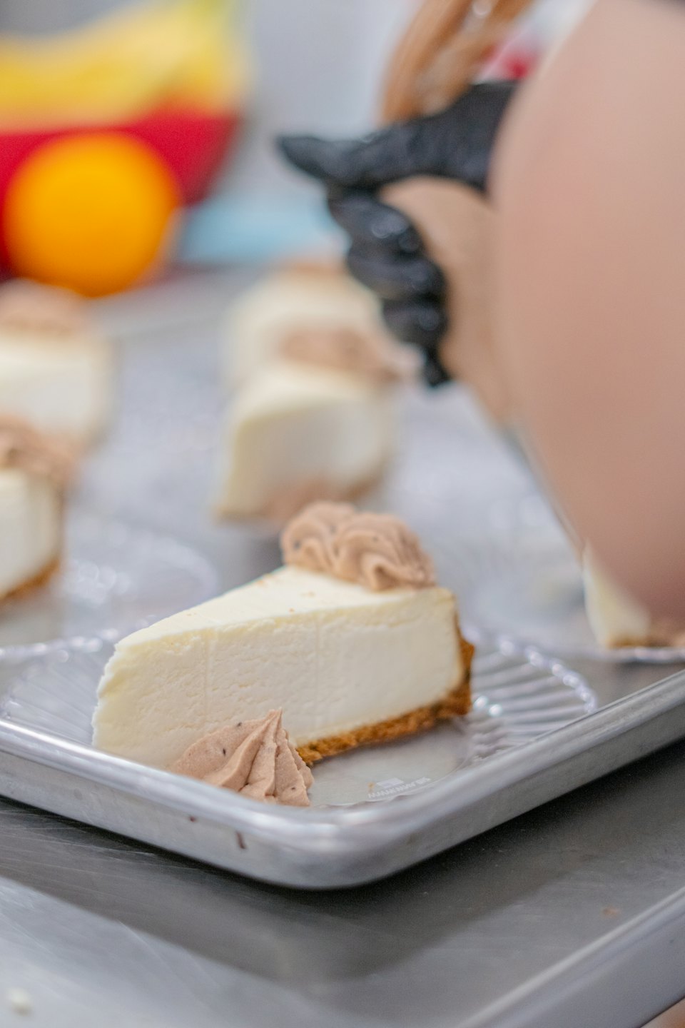 A baker pipes chocolate cream onto slices of cheesecake.