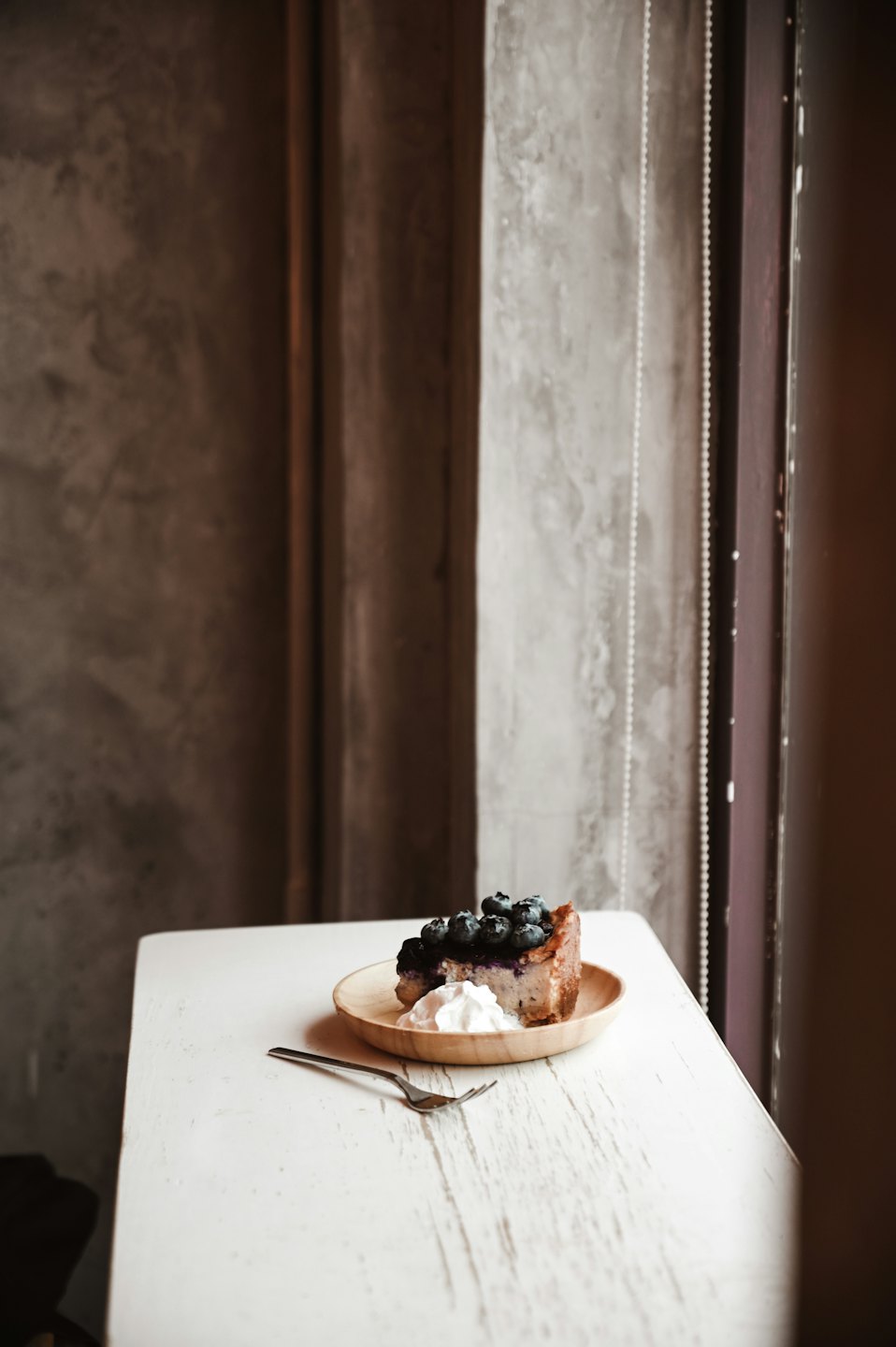 A slice of blueberry cheesecake with whipped cream on a wooden plate.